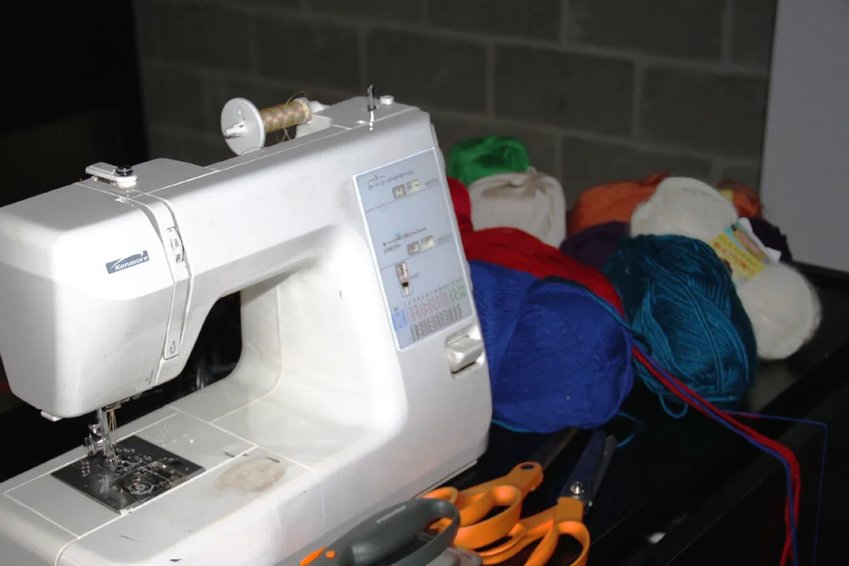A domestic sewing machine on a dark table beside a heap of coloured yarn, scissors and a seam ripper.