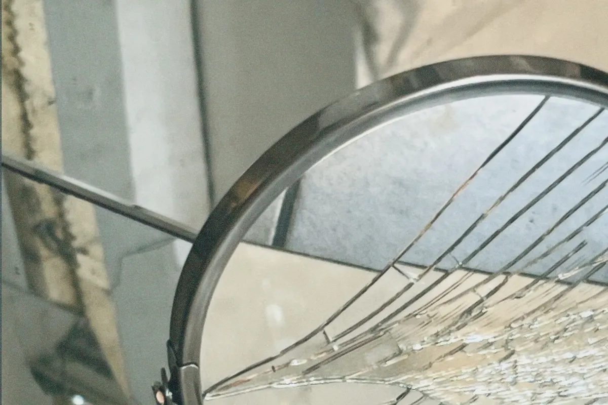 A round mirror cracked into long radiating shards but still held in place inside its slim metal frame, propped against a wall.