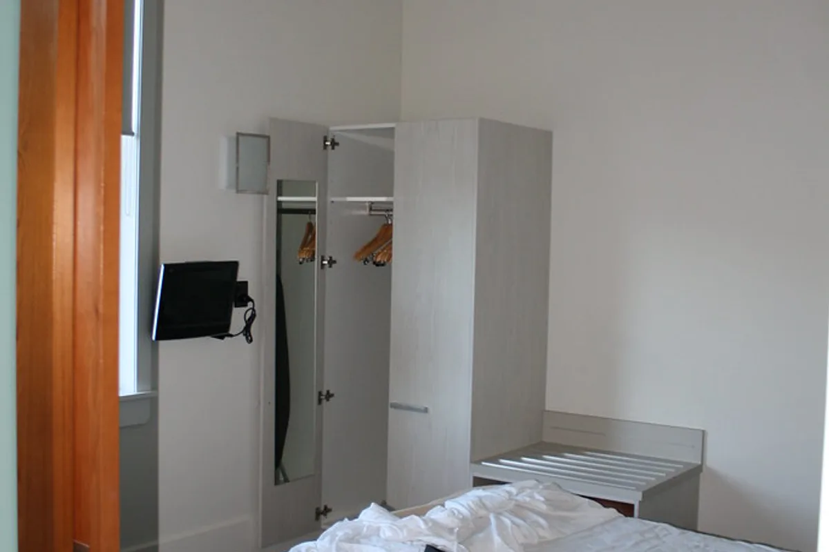A small television on an articulating wall mount in a bedroom, positioned beside a wardrobe beneath a ceiling fan.