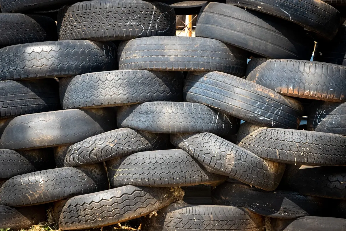 A wall of used car tyres stacked in overlapping rows outdoors in strong daylight.