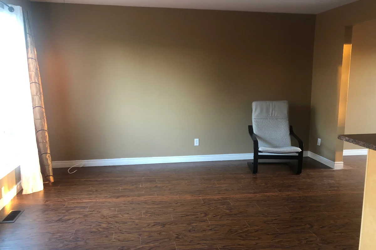 Nearly cleared residential living room with a lone armchair remaining on dark polished wooden flooring.