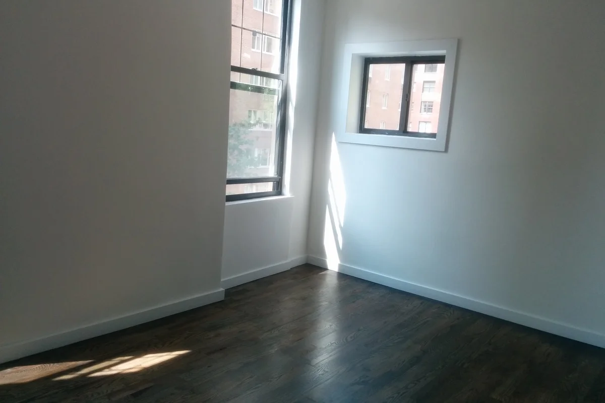 Completely cleared apartment room corner showing spotless dark wooden floors and clean painted white walls.
