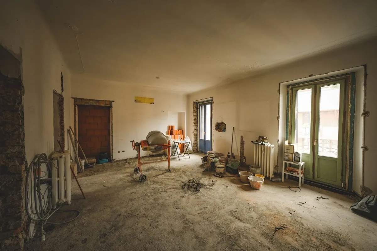 An empty room with bare plaster walls, exposed floor and a few tools where the contents have been cleared ahead of renovation work.