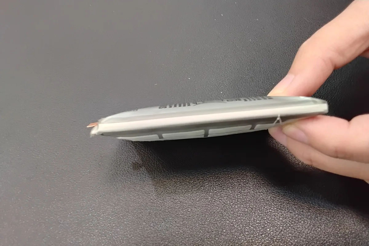A hand holding a visibly swollen flat lithium battery pack, its casing bulging along the edge.