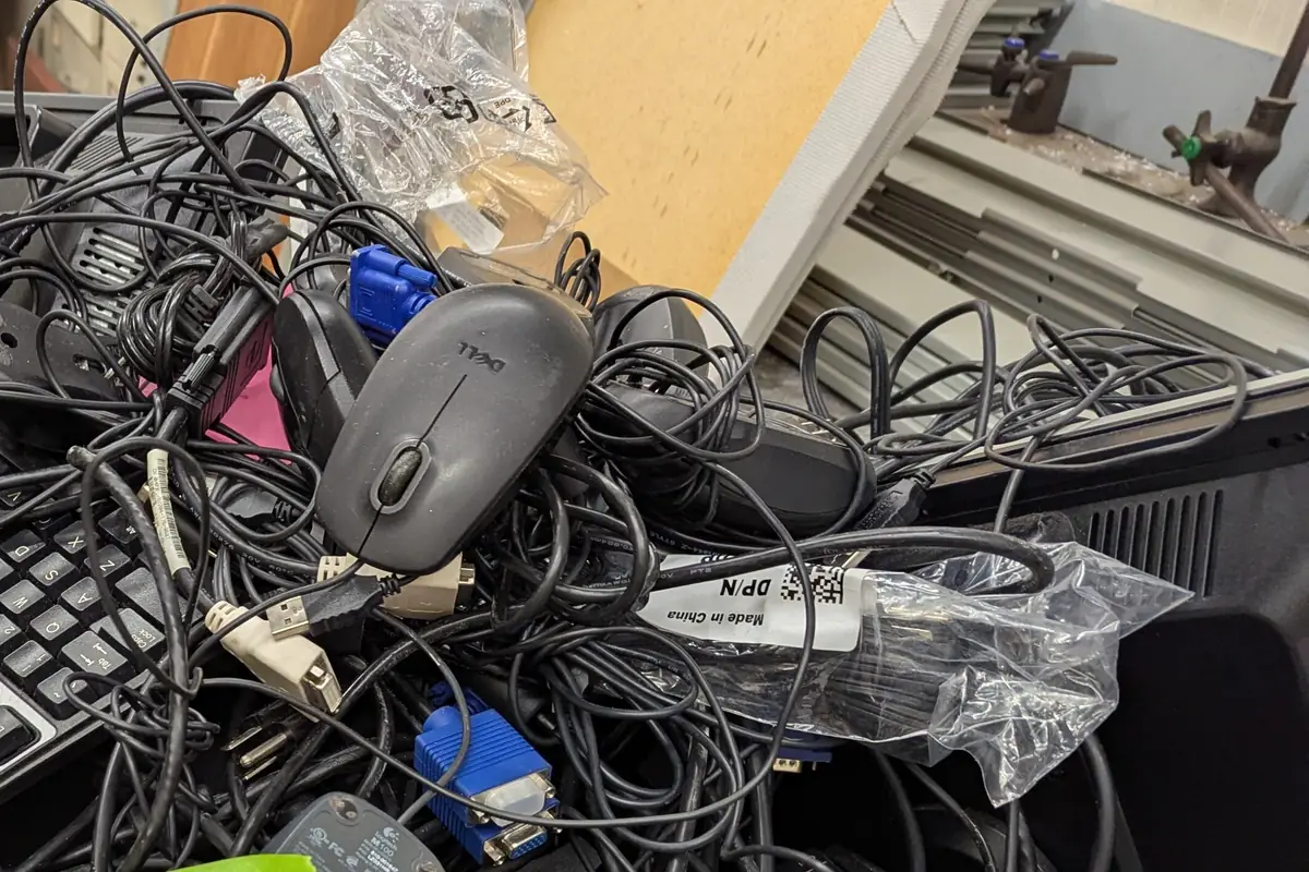 A tangle of black power cables, blue VGA connectors, computer mice and keyboards heaped together ready for disposal.