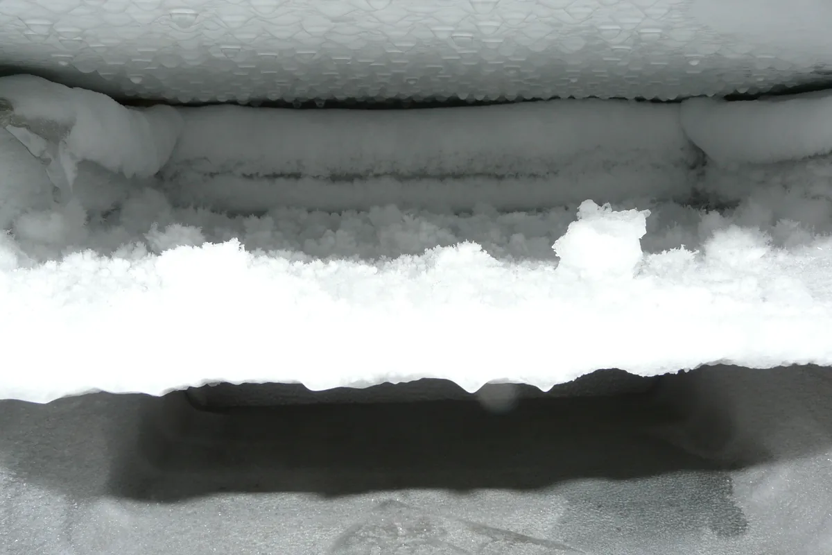 Heavy layers of white frost and ice built up across the interior walls and lid seal of a freezer during defrosting.