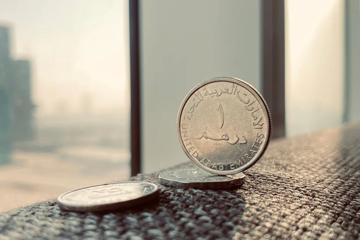 UAE dirham coins standing on a windowsill with the Dubai skyline blurred in the background.