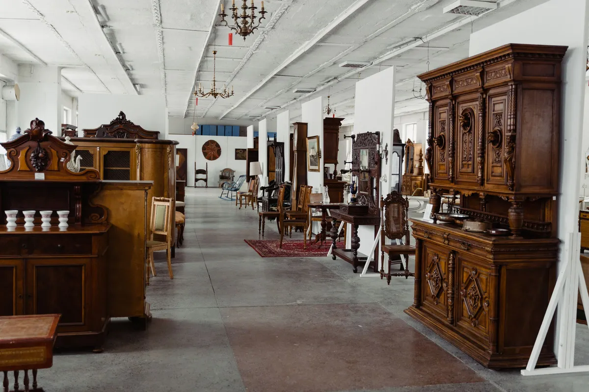 A long warehouse aisle lined with second-hand solid wood cabinets, dressers and chairs on a polished concrete floor.