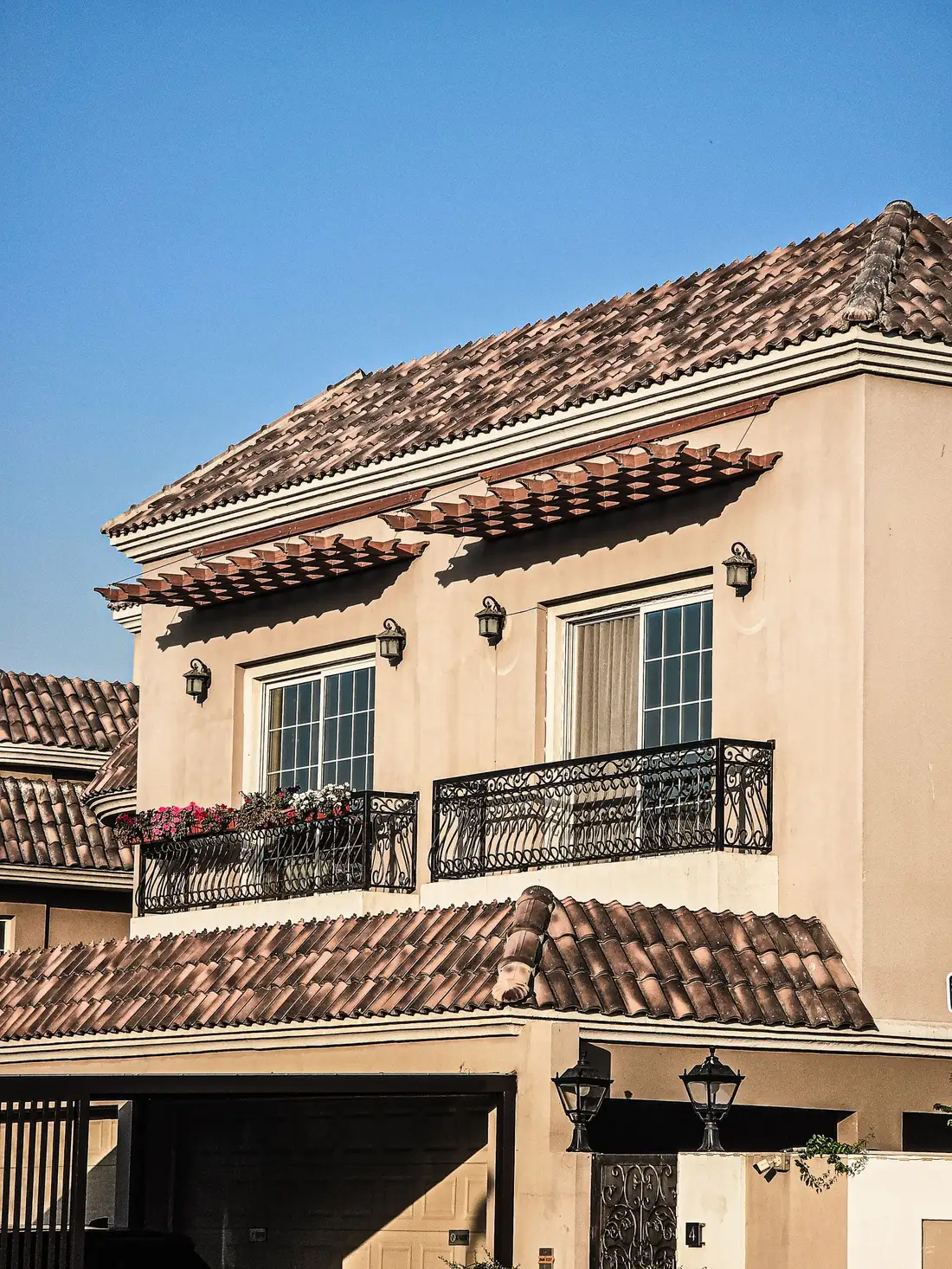 A two-storey Mediterranean-style villa with a tiled roof, balconies and a ground-floor garage in a gated Dubai community.