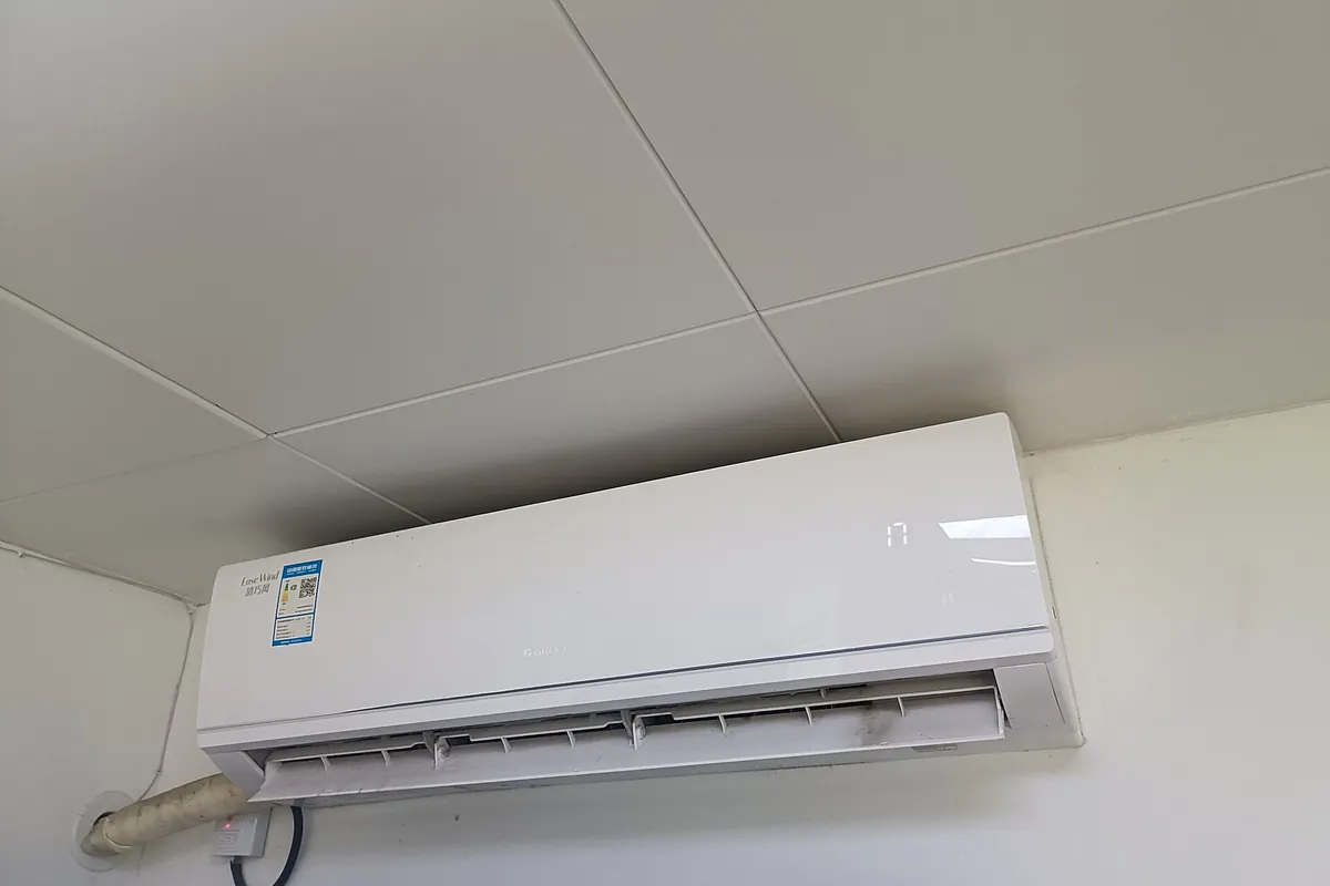 A wall-mounted split air conditioner indoor unit with its lagged pipe run passing through the wall above a switched isolator.
