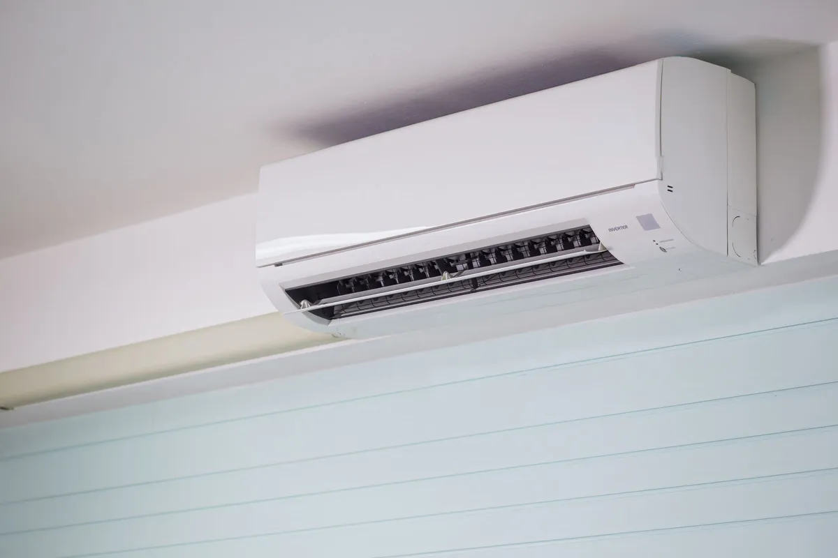 A white wall-mounted split air conditioning unit fitted high on an interior wall just below the ceiling, with its vent open.
