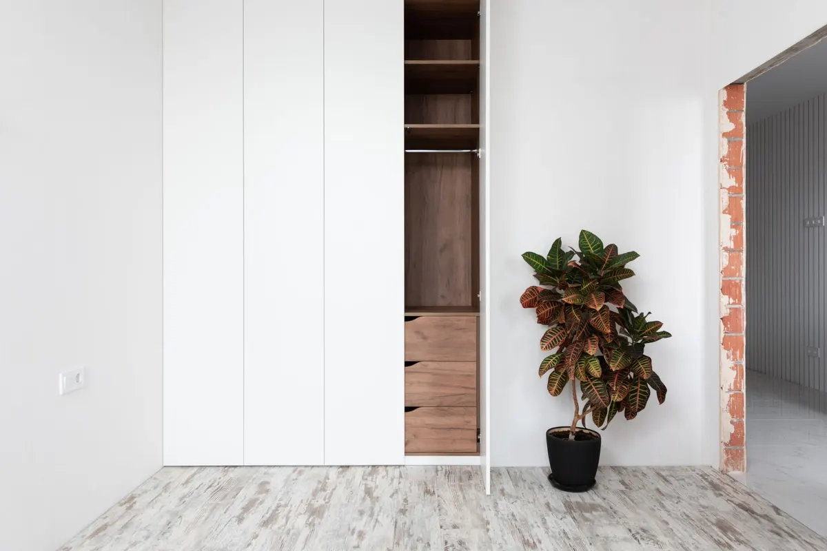 A floor-to-ceiling white wardrobe with one door open, revealing a walnut-coloured interior with shelves, a hanging rail and drawers.