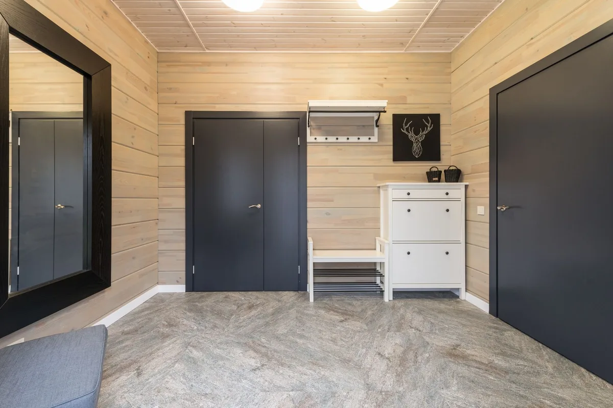 A white two-drawer shoe cabinet with a slatted shelf beneath, standing next to a wall-mounted coat hook shelf in an apartment entryway.