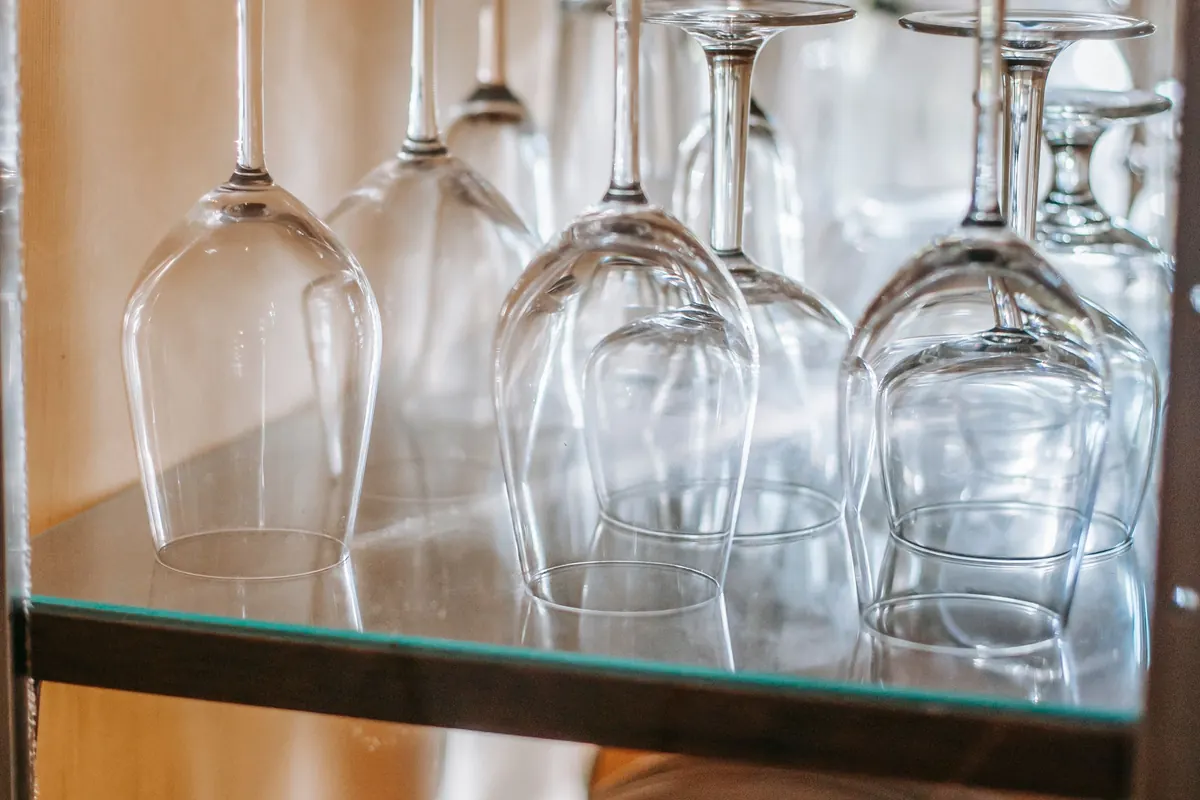 Wine glasses standing upside down on a glass shelf inside a wooden cabinet, lit from the side.