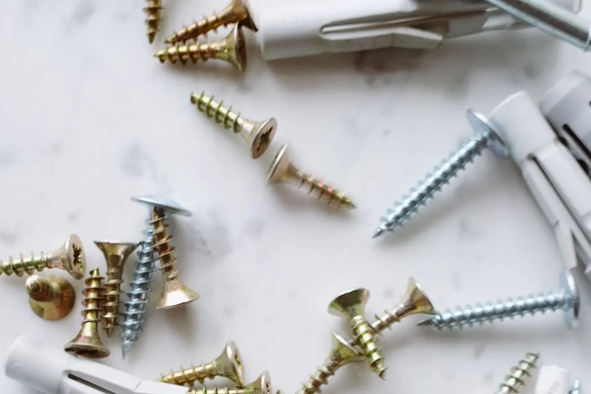 Brass and steel wood screws scattered with white plastic wall plugs across a pale marble surface.
