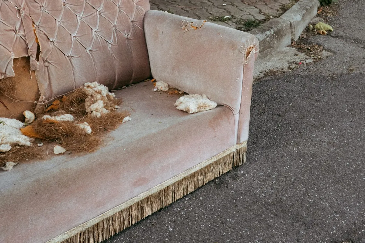 A badly damaged pink velvet sofa abandoned at the kerbside, with torn upholstery and stuffing spilling out of the seat.